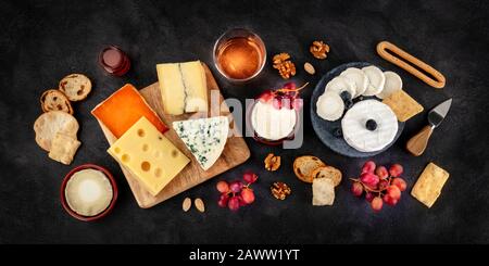 Panorama di varietà di formaggi con vino e frutta, un piatto, colpo di testa su uno sfondo nero Foto Stock