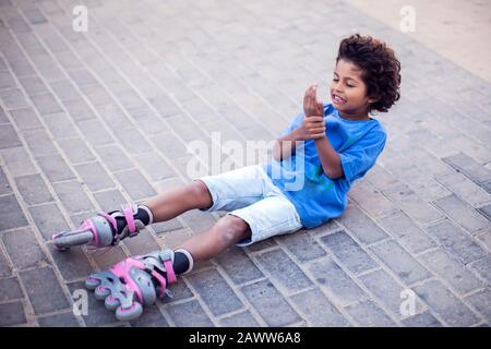 Un ragazzo su rollerskates si è abbassato e si sente dolore. Bambini, leasure e concetto di assistenza sanitaria Foto Stock