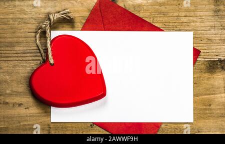 Cuore rosso con carta bianca e busta rossa su sfondo di legno. Concetto di San Valentino con spazio per testo o foto. Foto Stock