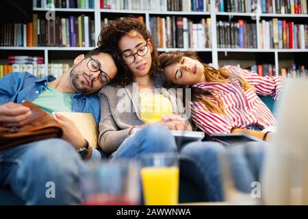 College, studio, università e concetto di istruzione. Gruppo di studenti stanchi che imparano in biblioteca Foto Stock