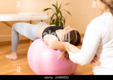 Fisioterapista lavorare con giovani femmine client sulla forza di base utilizzando fitball. Riabilitazione e Fisioterapia sfondo. Foto Stock