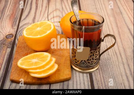 Tè in un bicchiere sfaccettato in un bicchiere d'annata, limone affettato su una tavola su sfondo di legno. Primo piano Foto Stock