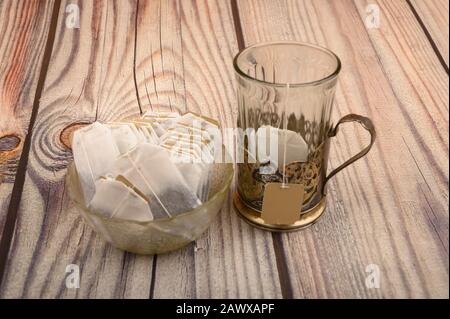 Bustine di tè in vaso di vetro e un bicchiere sfaccettato vuoto in una tazza d'epoca su sfondo di legno. Primo piano Foto Stock