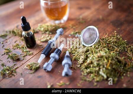 Concetto di marijuana medica - olio CBD, pasta CBD, foglie di marijuana secca. Iniezione di olio CBD, pasta CBD, foglie di marijuana secca su sfondo di legno. Foto Stock