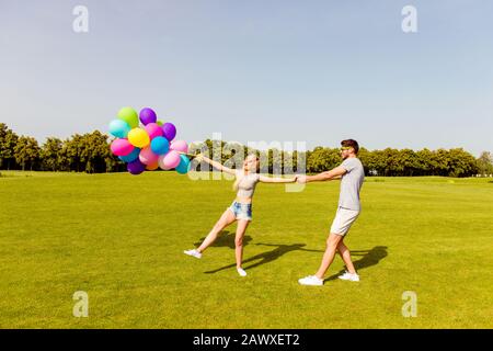 Giovane uomo felice che porta la sua ragazza con palloncini Foto Stock
