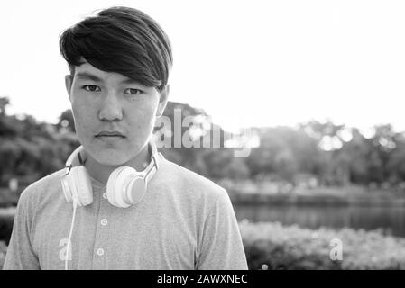 Giovane ragazzo asiatico teenage indossa le cuffie mentre si rilassa al parco Foto Stock