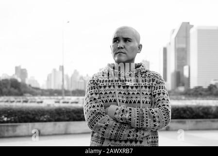 Giovani asiatici calvo uomo contro la vista della città al parco Foto Stock