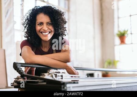 Giovane donna sorridente appoggiata su un banco da lavoro nel suo studio Foto Stock