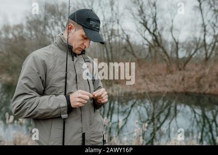 Pescando l'uomo, levandosi in piedi sulla riva del fiume in una giornata torbida Foto Stock