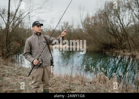 Pescando l'uomo, levandosi in piedi sulla riva del fiume in una giornata torbida Foto Stock