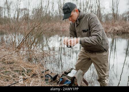 Pescando l'uomo, levandosi in piedi sulla riva del fiume in una giornata torbida Foto Stock