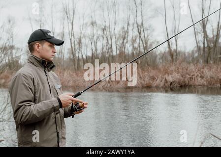 Pesca dell'uomo, in piedi sulla riva del fiume in una giornata torbida Foto Stock