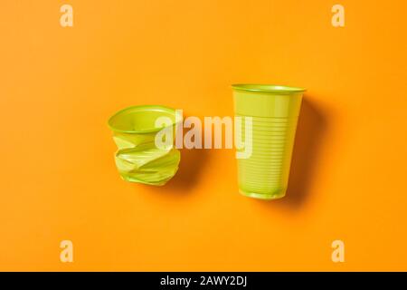 Orizzontale da sopra piatto scatto di posa usa monouso e nuove tazze di plastica verde su sfondo arancione brillante Foto Stock