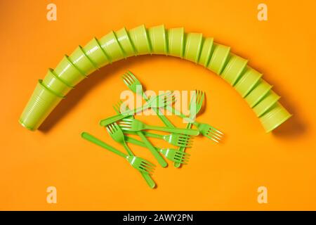 Piatto concettuale di un set di tazze monouso in plastica verde chiaro e forchette su sfondo arancione brillante Foto Stock