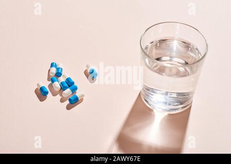 Capsule in pillole bianche E blu e vetro d'acqua su superficie del tavolo rosa pallido, colpo orizzontale Foto Stock