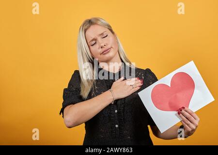 ragazza in abito nero deluso triste donna che tiene pezzo di carta con cuore rosso Foto Stock