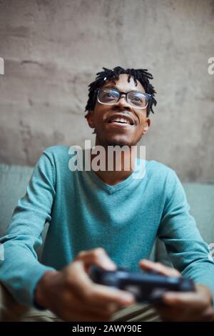 Ritratto a basso angolo di uomo sorridente afro-americano che gioca ai videogiochi tramite console di gioco Foto Stock