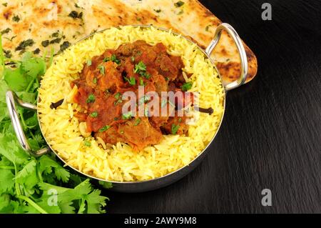 Agnello rogan josh curry pasto con riso pilau e pane naan su uno sfondo di pietra ardesia Foto Stock