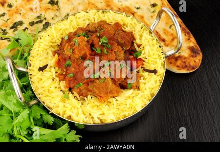 Agnello rogan josh curry pasto con riso pilau e pane naan su uno sfondo di pietra ardesia Foto Stock