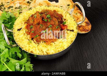 Agnello rogan josh curry pasto con riso pilau e pane naan su uno sfondo di pietra ardesia Foto Stock