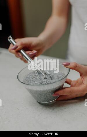 Donna Che Mescola Budino Di Chia In Ciotola Di Vetro In Cucina Foto Stock