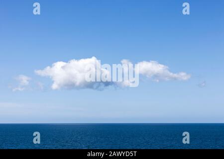 Le nuvole di Cumulus si formano in un cielo azzurro chiaro su un orizzonte calmo dell'oceano Foto Stock