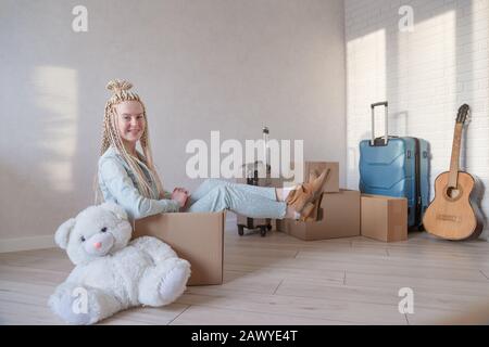 giovane donna straordinaria è pronta a muoversi. Si siede in una scatola. Valigie confezionate e articoli confezionati in background. Foto Stock
