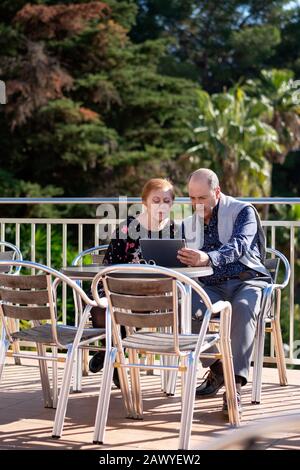 Coppia in pensione seduta sulla terrazza all'aperto che guarda preoccupato per il portatile Foto Stock