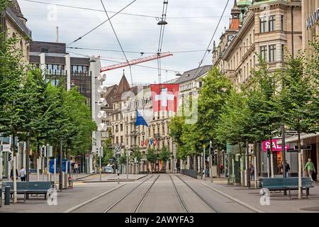 Zurigo, Svizzera - 10 giugno 2017: Passeggiata per lo shopping Bahnhofstrasse, città interna di Zurigo. Bandiera svizzera e binari ferroviari tram di fronte. Foto Stock