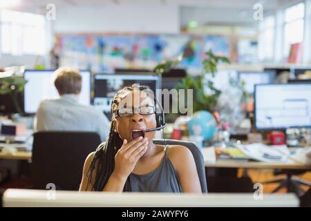Donna d'affari stanco con l'auricolare che sbava al computer in ufficio open space Foto Stock