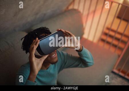 Vista ad alto angolo su un uomo afro-americano che indossa gli attrezzi VR mentre ti godi un'esperienza immersiva in interni futuristici, spazio per le copie Foto Stock