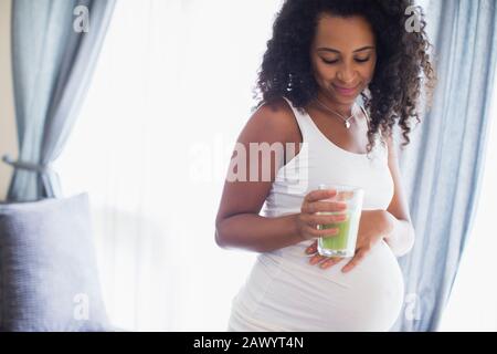 Giovane donna incinta bere frullato verde Foto Stock