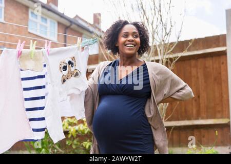 Felice donna incinta appesa lavanderia sulla linea di stendibiancheria in giardino Foto Stock