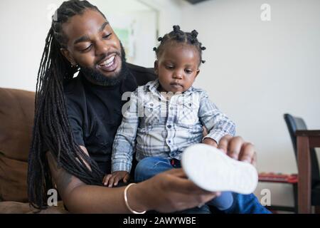 Padre con le trecce lunghe che mettono le scarpe sul figlio del toddler Foto Stock