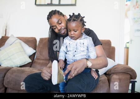 Il padre che mette le scarpe sul figlio del toddler sul divano Foto Stock