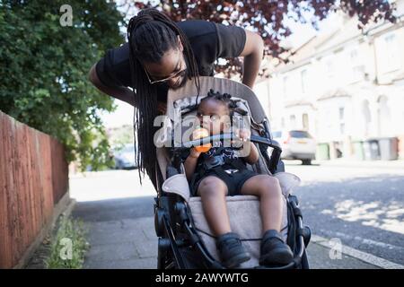 Il padre spinge il figlio del toddler in passeggino sul marciapiede urbano Foto Stock