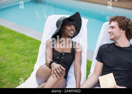 Coppia giovane e felice che si rilassa nelle sedie a sdraio a bordo piscina Foto Stock