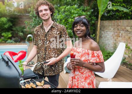Ritratto felice giovane coppia barbecue a bordo piscina Foto Stock