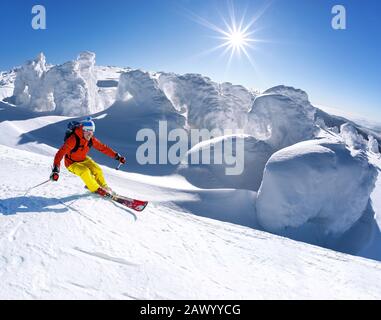 Sciatore in discesa sugli sci in alta montagna contro il cielo blu Foto Stock