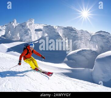 Sciatore in discesa sugli sci in alta montagna contro il cielo blu Foto Stock