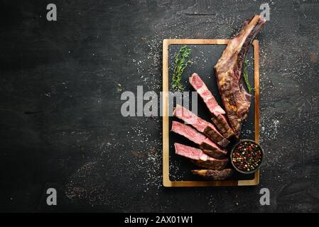 Bistecca alla griglia sull'osso tagliata, erbe e spezie su sfondo di legno. Barbecue. Vista dall'alto. Spazio libero per il testo. Foto Stock