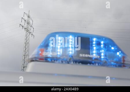 Duisburg, Germania. 10th Feb, 2020. Un'auto di polizia con una luce blu si trova davanti a un polo di alimentazione, dove c'è un problema con la linea ad alta tensione che attraversa il Reno. Inizialmente, un cavo di messa a terra innocuo era caduto nell'acqua sul lato Krefeld, che potrebbe portare ad un cavo con tensione, secondo la polizia di Duisburg. Il fiume è stato chiuso per la navigazione tra Düsseldorf e Krefeld. Al momento, non si può né confermare né negare se il caso comporti danni da tempesta. Credito: David Young/Dpa/Alamy Live News Foto Stock