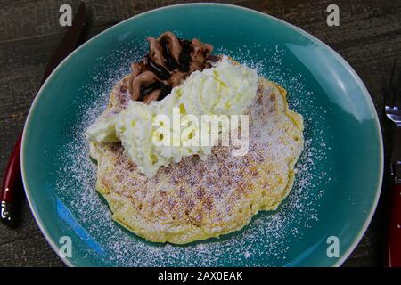 Primo piano con waffle freschi ricoperti di zucchero a velo e gelato al cioccolato fondente su piastra blu per la cina Foto Stock