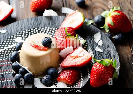 Tradizionale dessert italiano panna cotta, decorato con fragole e mirtilli su un piatto primo piano, fuoco selettivo Foto Stock