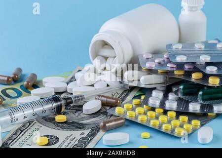 Le pillole mediche sono su un denaro su uno sfondo blu. Pillole mediche su fondo monetario come simbolo dei costi di assistenza sanitaria. Concetto di medicina Foto Stock