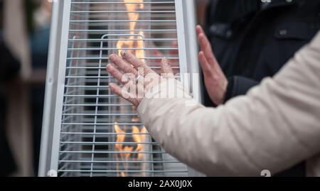 donna che si strarpano le mani davanti a un riscaldatore a gas Foto Stock