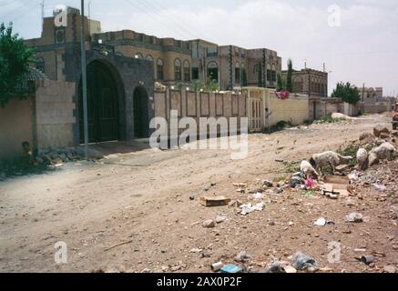 Sana'a, Yemen. 1994. Strada residenziale scena con rifiuti nella strada che viene mangiato da animali roaming. Un ragazzo è seduto contro il muro con il suo cane. Foto Stock