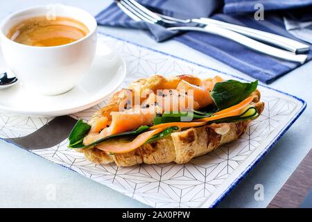 Concetto di colazione. Croissant con pesce rosso fresco salato, formaggio cremoso e verdure e una tazza di caffè. Foto Stock