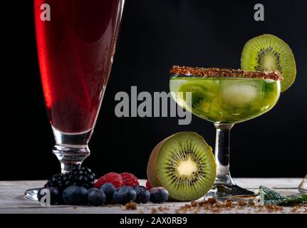 Cocktail Kiwi decorato con fette e frutti della foresta su una base di legno. Foto Stock
