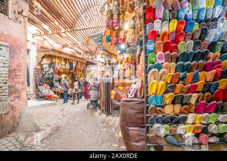 Strada stretta nella medina di Marrakech piena di negozi con pantofole in pelle Foto Stock